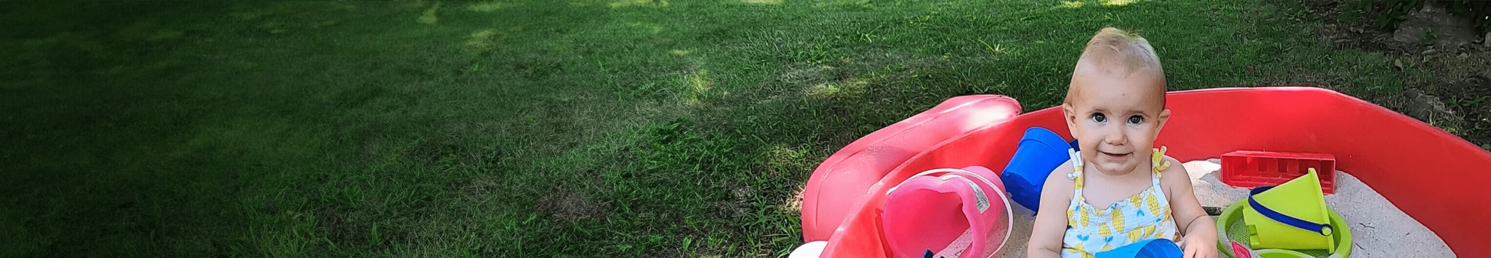 Smiling toddler girl plays in sandbox