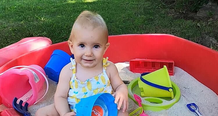 Smiling toddler girl plays in sandbox