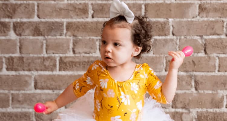 A little girl in a tutu, holding maracas, looking intently at something out of view