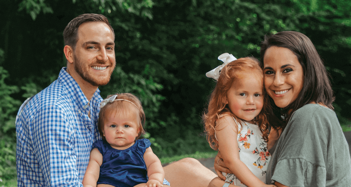 Two parents with their toddler and baby girls in a park-like area