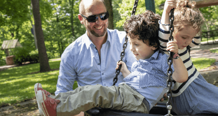 Father pushing two young children on a tire swing