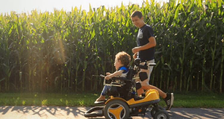 Young boy in wheelchair and young man in front of a cornfield