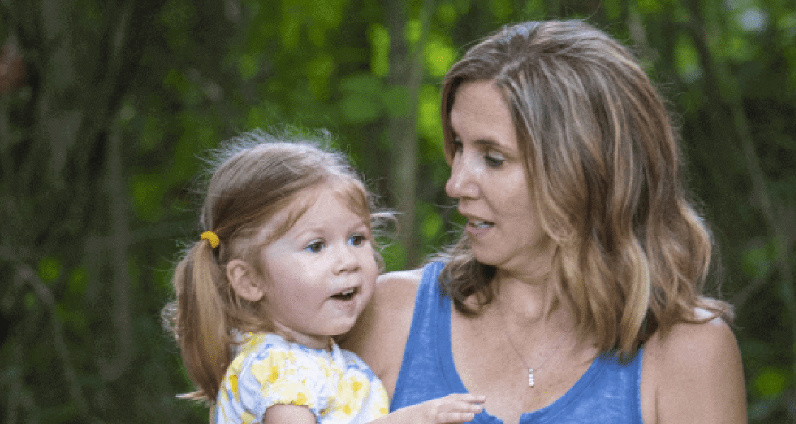 A mother holds her daughter in a leafy area