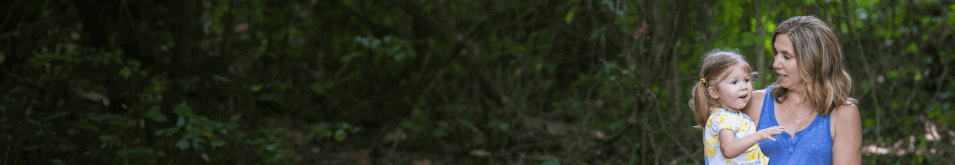 A mother holds her daughter in a leafy area