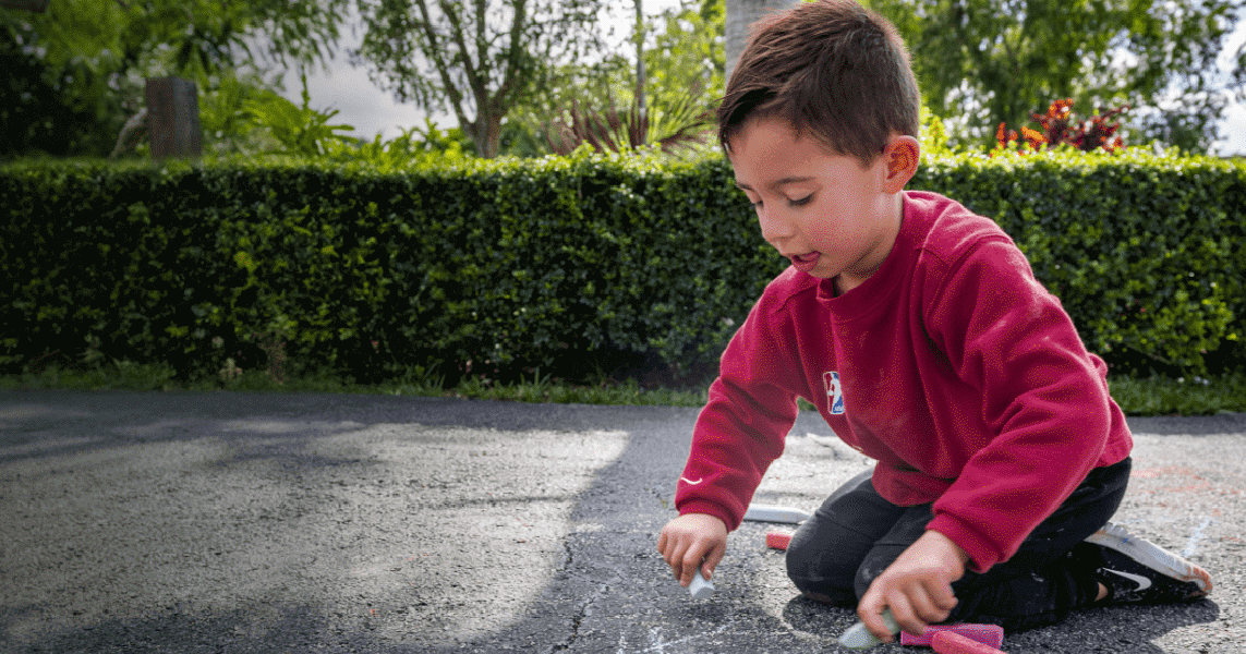 A young boy draws with chalk on a driveway