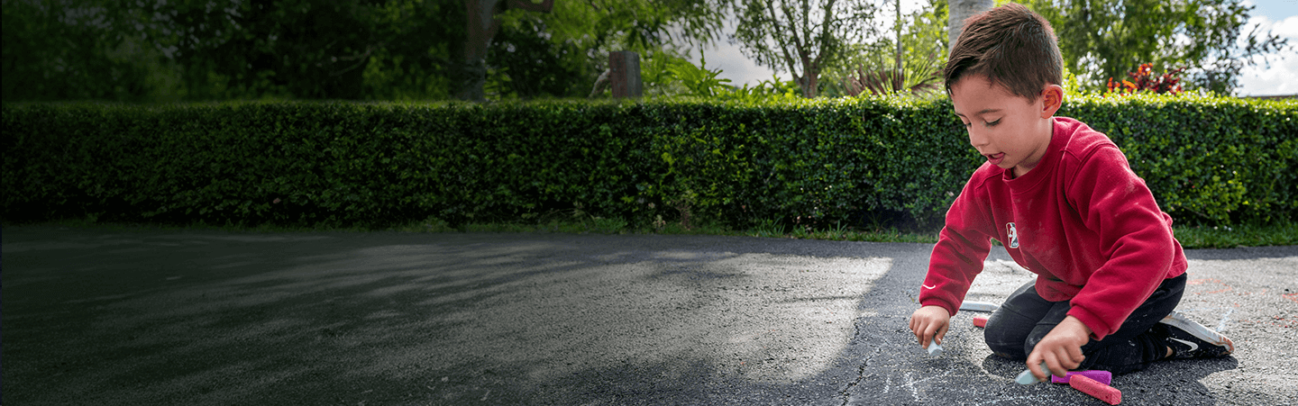 A young boy draws with chalk on a driveway